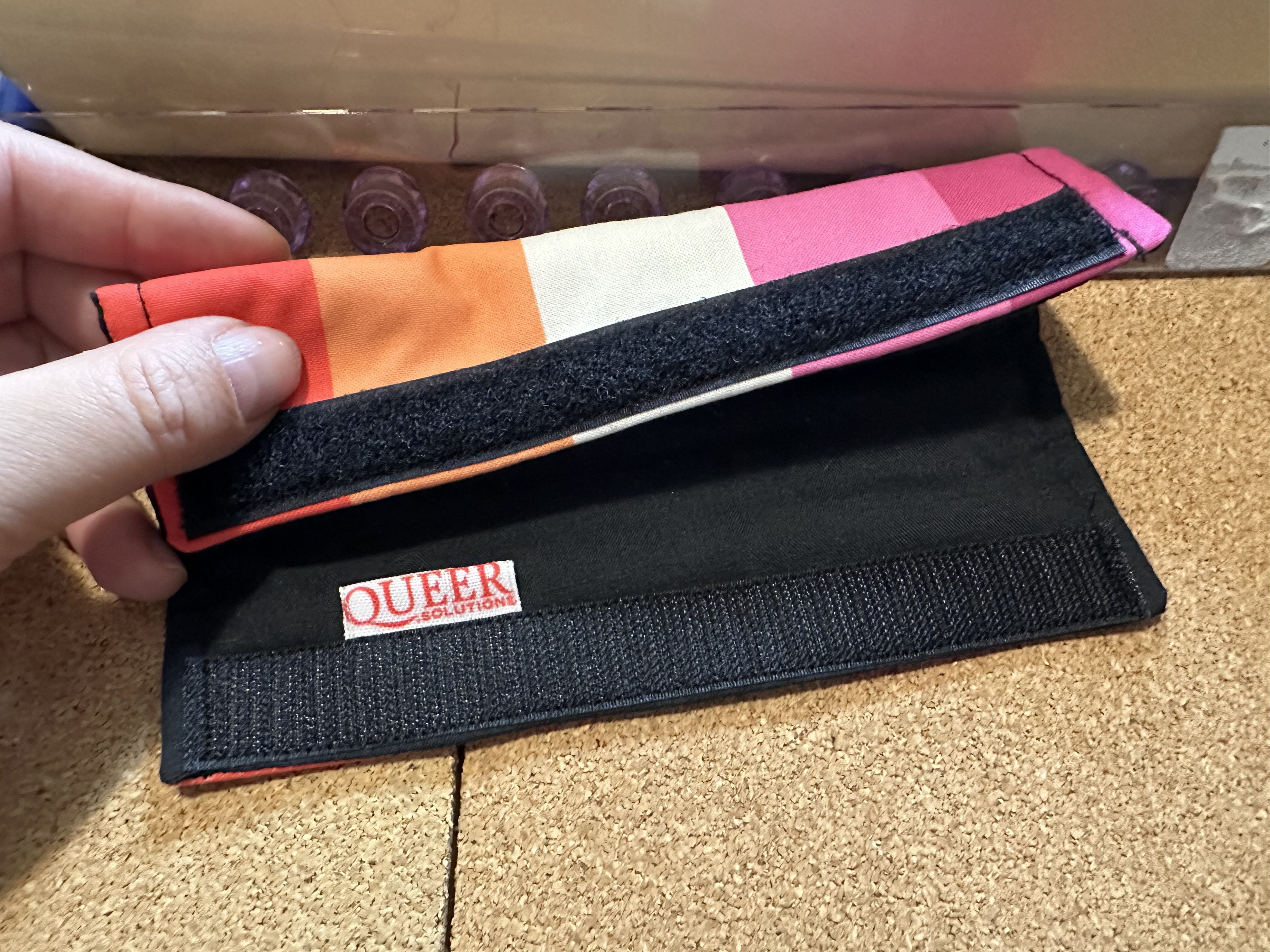 une des protections, drapeau de fierté lesbienne, que je tiens entrouverte pour montrer une étiquette Queer.solutions à l'intérieur