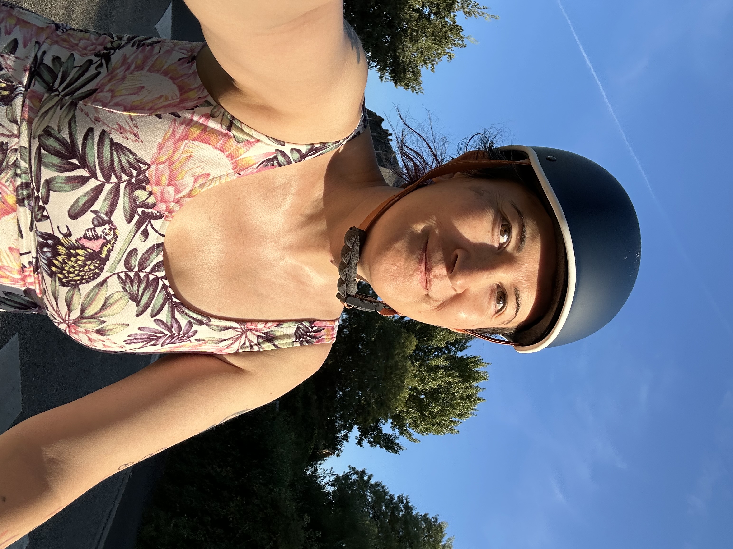 Autoportrait à vélo, je tiens le téléphone d'une main et le guidon de l'autre, et je porte un casque de vélo. La lumière dorée du coucher de soleil me donne une mine radieuse.