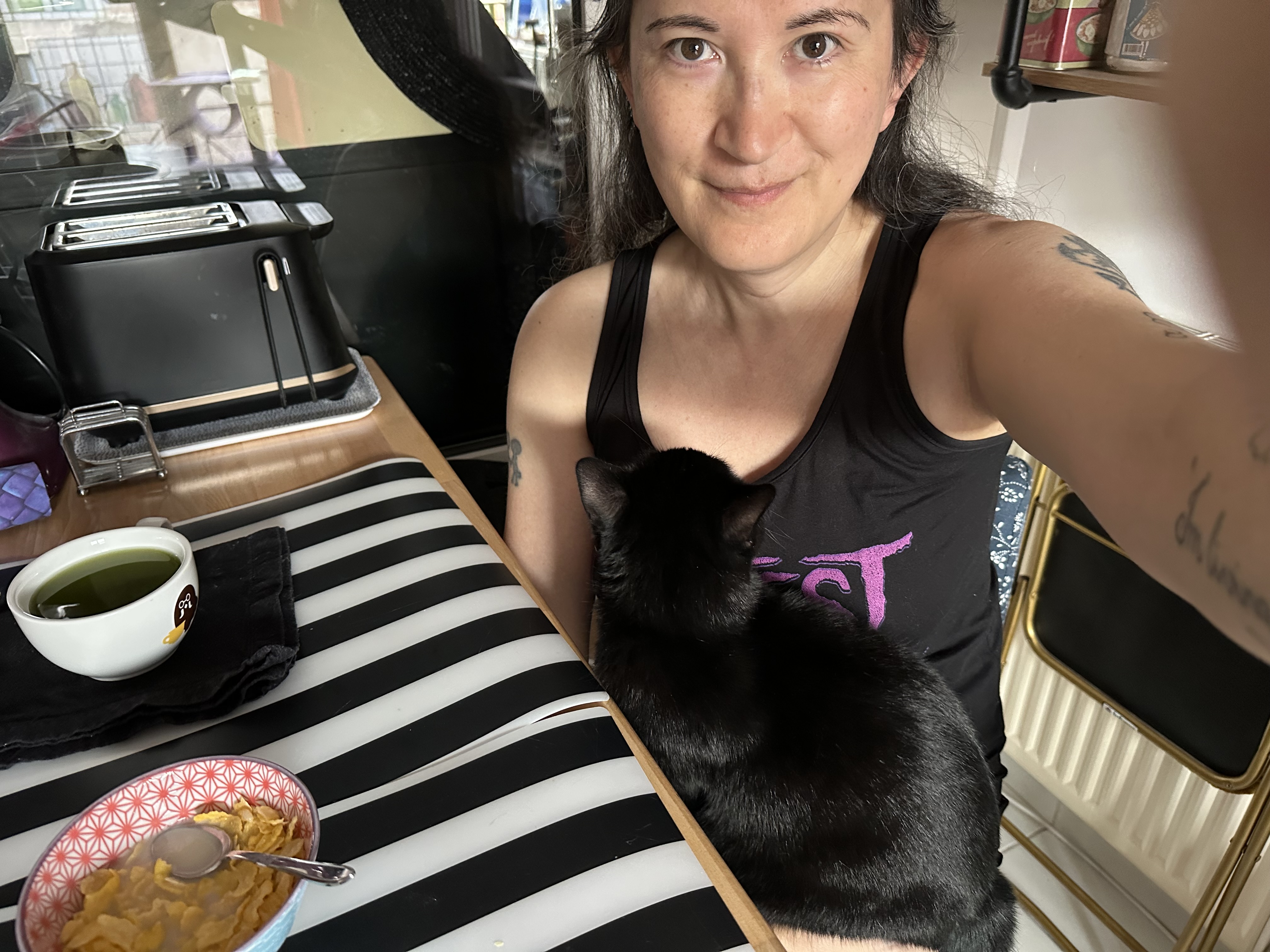 autoportrait avec une chatte noire sur les genoux, devant une table sur laquelle m'attendent une tasse de thé vert au matcha et un bol de céréales.
