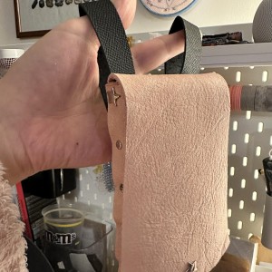 L’étui rose est suspendu à deux boucles de cuir noir qui s’accrocheront à ma ceinture arc en ciel. Sur le mur du fond, deux jolies broderies maison.