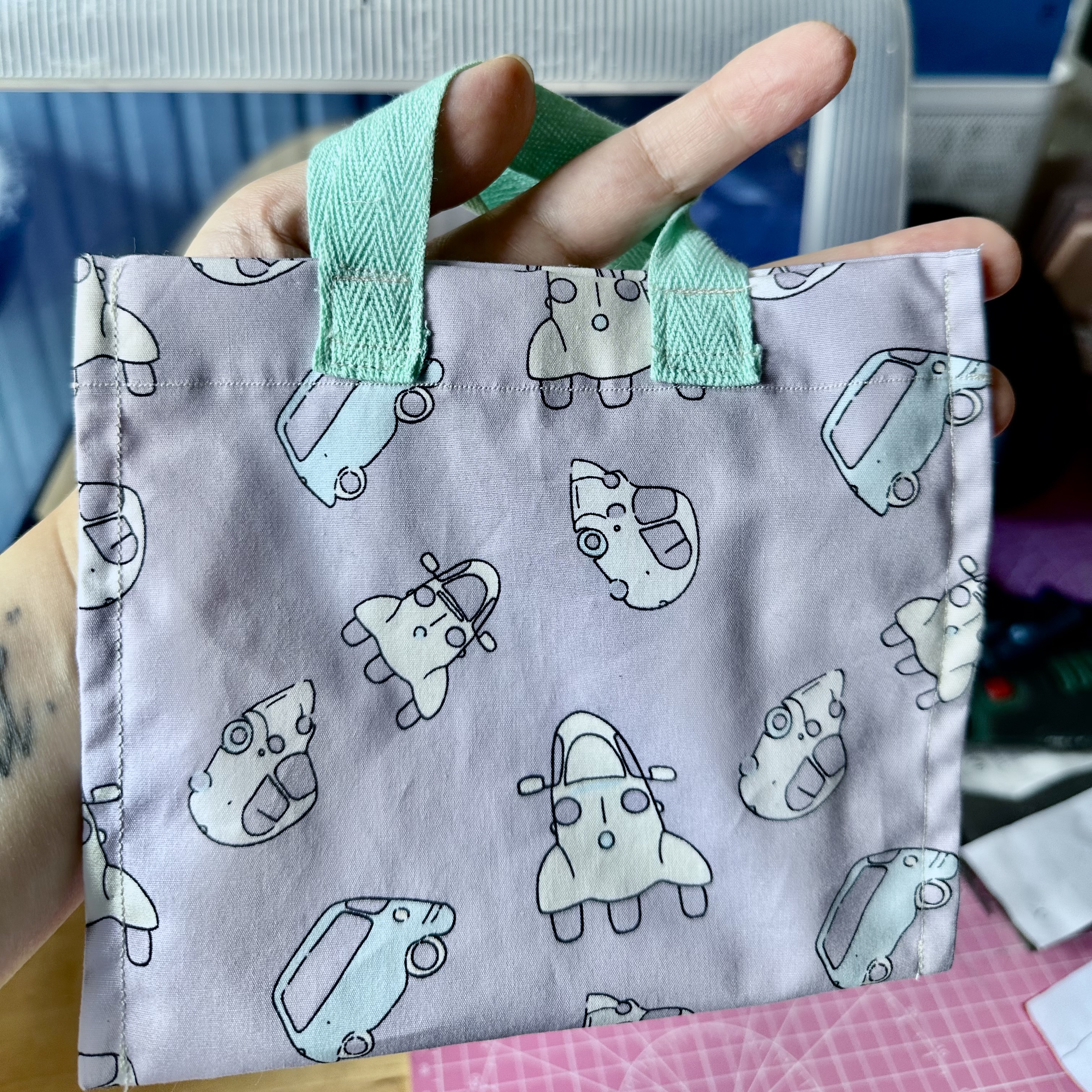 vu de face d'un sac violet avec des petites voitures. Environ 15cm de large.