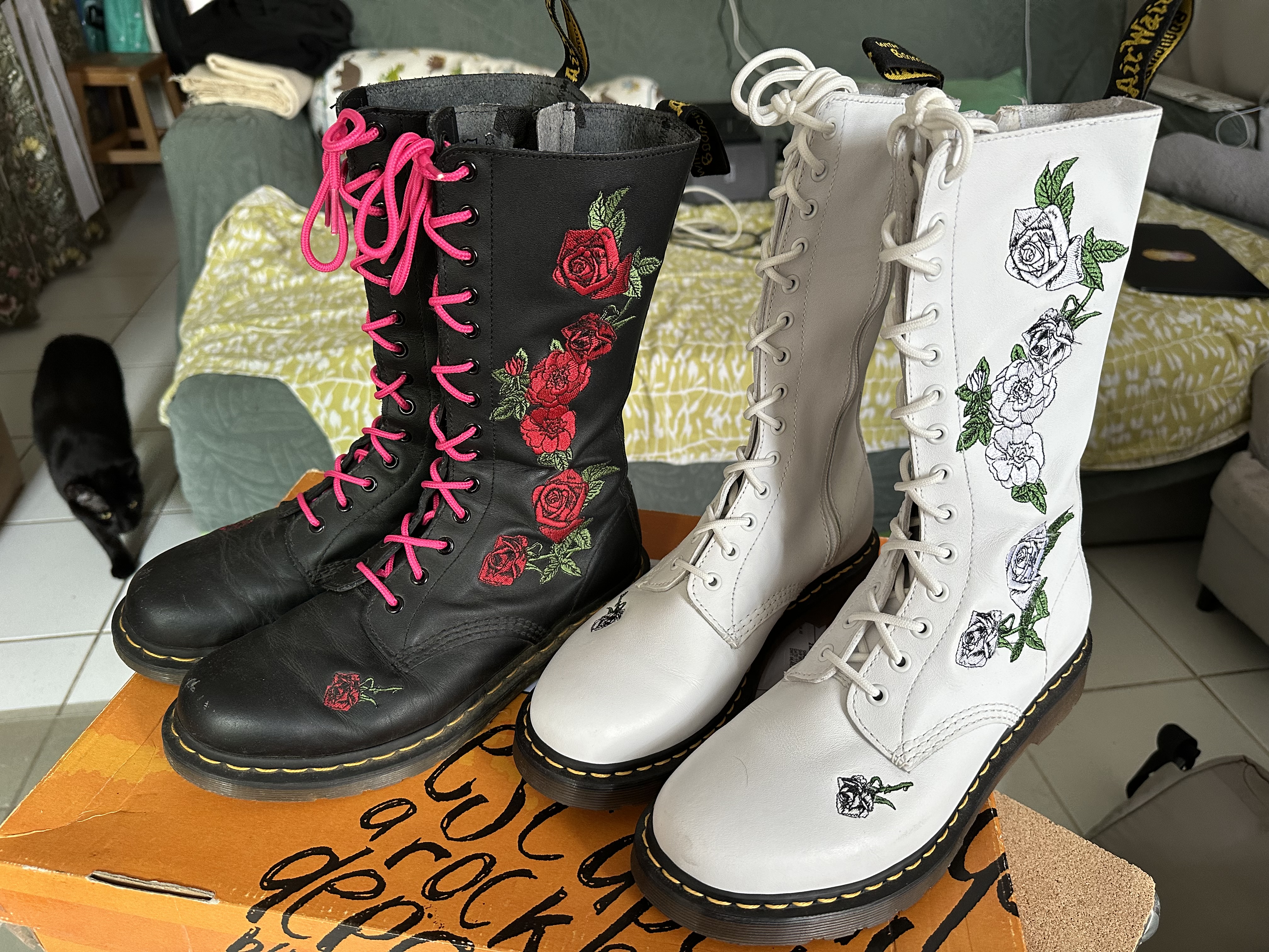 Deux paires de bottes Vonda de Dr Martens, une noire et une blanche. Les deux sont brodées avec de magnifiques roses rouges sur les bottes noires, et argentées sur les bottes blanches.